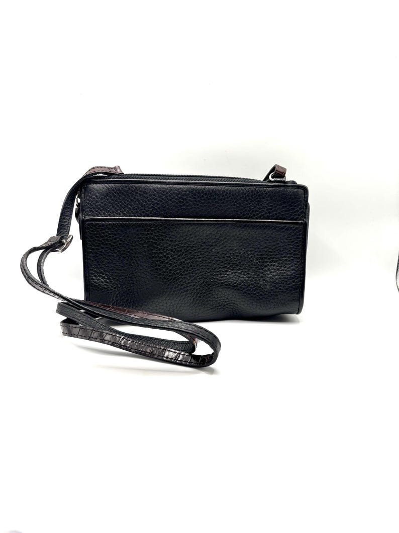 May include: Black leather crossbody bag with a long, adjustable strap. The bag has a rectangular shape with a zippered top and a textured surface. The strap features a brown and black pattern.