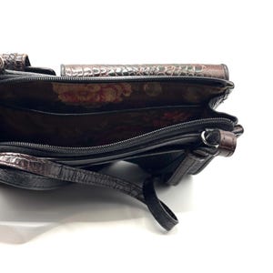 May include: Black and brown leather crossbody bag with a crocodile-like texture. The bag has a floral patterned interior and a long strap. The bag is open, revealing multiple compartments and a zipper closure.