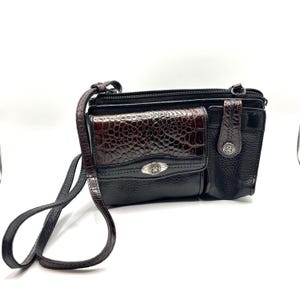 May include: Black crossbody bag with a brown, faux-crocodile skin flap and accents. The bag has a long, adjustable strap and multiple compartments. Silver-toned hardware accents the bag's design.
