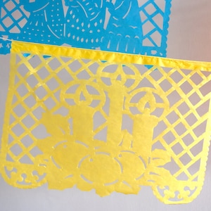 May include: A yellow paper banner with a cut-out design of flowers and leaves. The banner is strung with white string and is part of a larger garland of colourful banners.