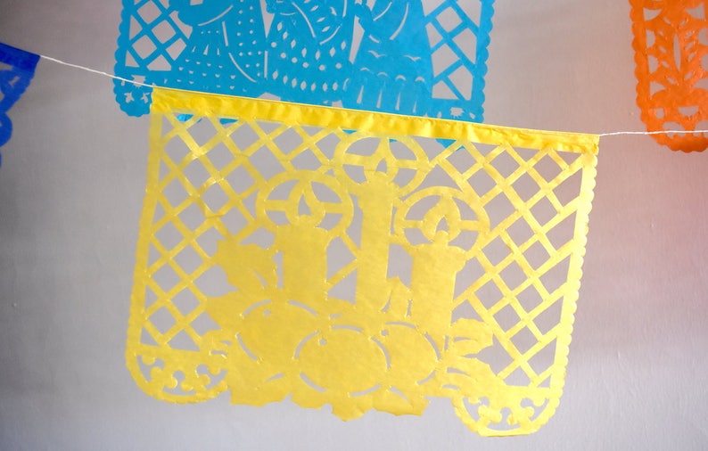 May include: A yellow paper banner with a cut-out design of flowers and leaves. The banner is strung with white string and is part of a larger garland of colourful banners.