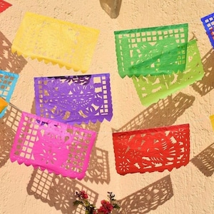 May include: A collection of colourful paper decorations with intricate cutouts, hanging on a wall. The decorations are in various colours, including yellow, green, purple, pink, and red.