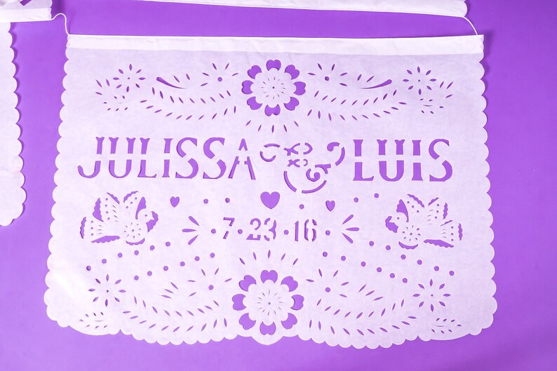 Puede incluir: Bandera de papel blanco con intrincados dise&ntilde;os recortados, incluyendo flores, p&aacute;jaros y corazones. La bandera dice "Julissa & Luis 7.23.16".