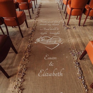 May include: A burlap aisle runner with the words "I take your hand inside my hand and hold it tight tonight" printed on it. The runner also features a heart with musical notes, the names "Euan & Elizabeth", and the date "19.11.16".