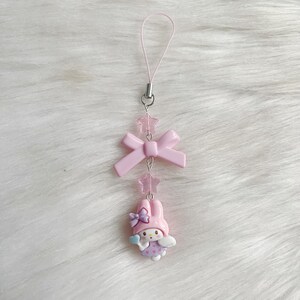 May include: Pink phone charm with a pink bow, pink stars, and a pink and white cartoon character with wings.