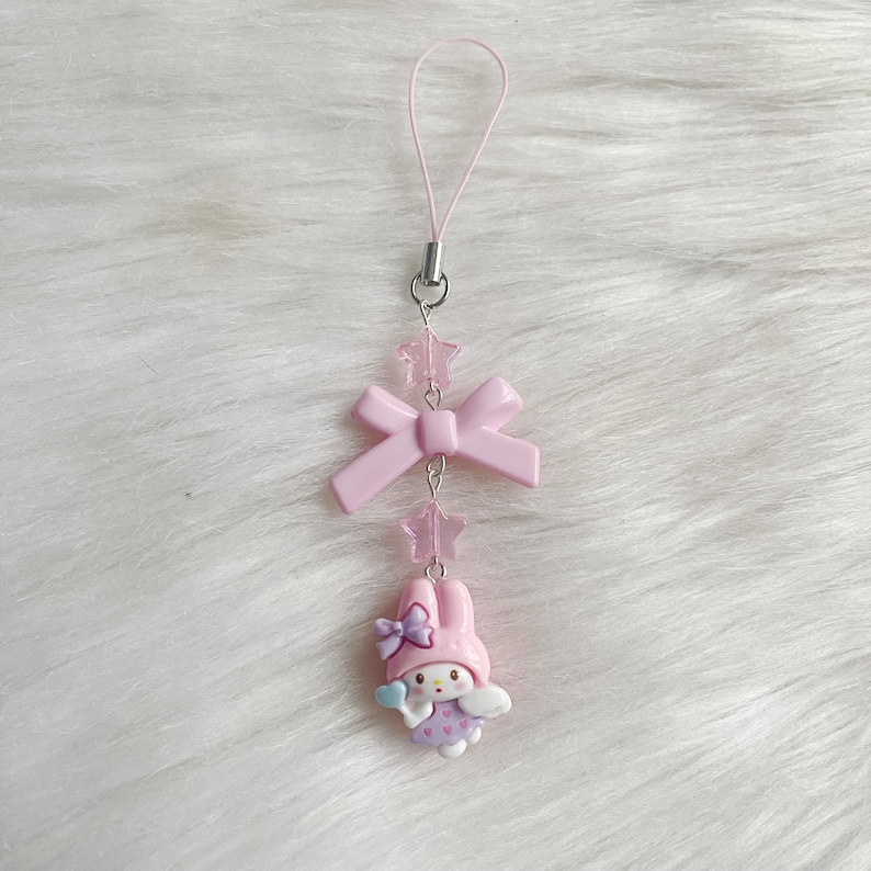 May include: Pink phone charm with a pink bow, pink stars, and a pink and white cartoon character with wings.