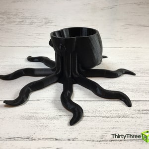 May include: A black 3D printed octopus planter with a round pot on top. The octopus has eight tentacles.