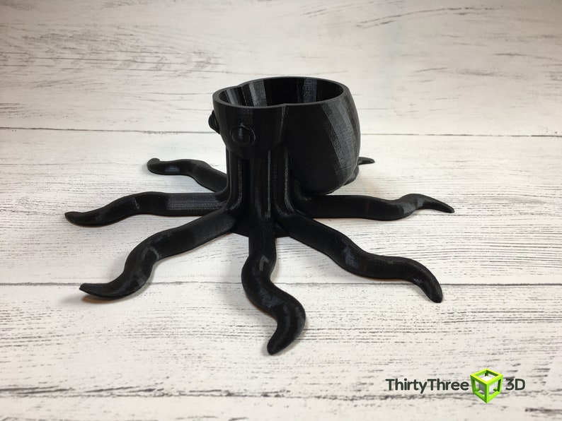 May include: A black 3D printed octopus planter with a round pot on top. The octopus has eight tentacles.
