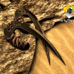 May include: Two black curved throwing knives with brown leather wrappings on the handles. The knives are lying on a brown and tan textured surface.
