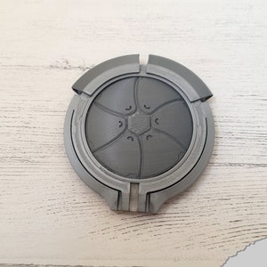 May include: A gray 3D printed circular object with a design of a flower with five petals and a center with a hexagonal shape.