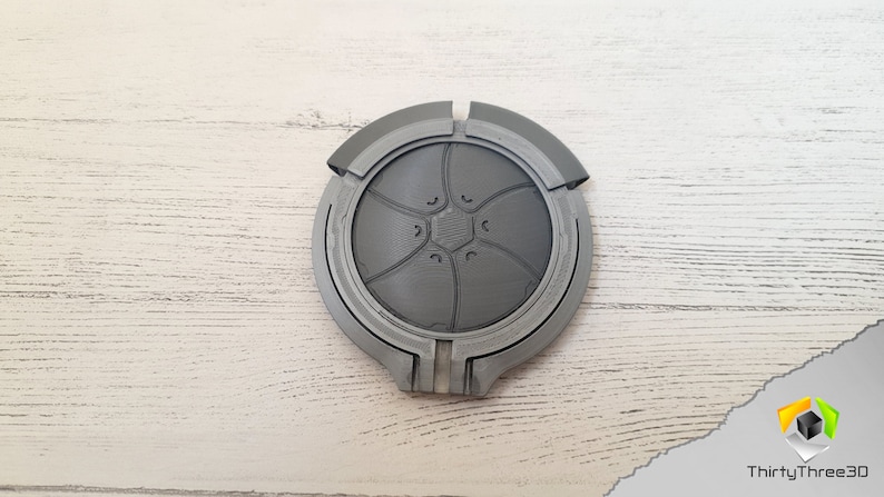 May include: A gray 3D printed circular object with a design of a flower with five petals and a center with a hexagonal shape.