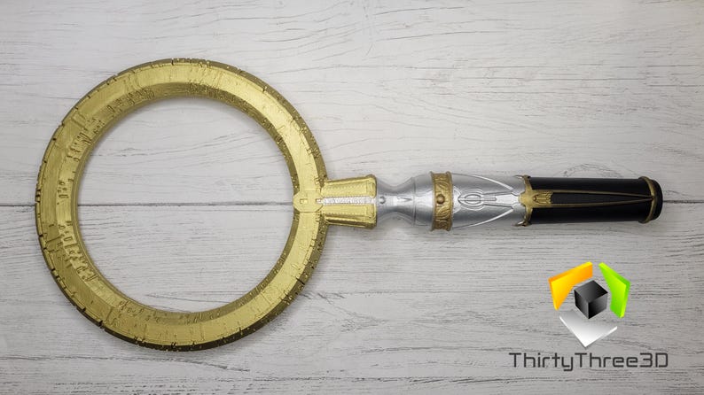 Pode incluir: Uma chave decorativa circular dourada com marcas intrincadas e uma al&ccedil;a prateada e preta.