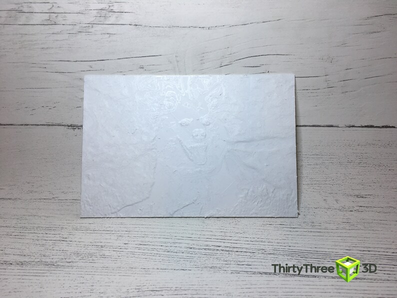 May include: A white, textured, rectangular card with a raised, embossed image of a snarling face.