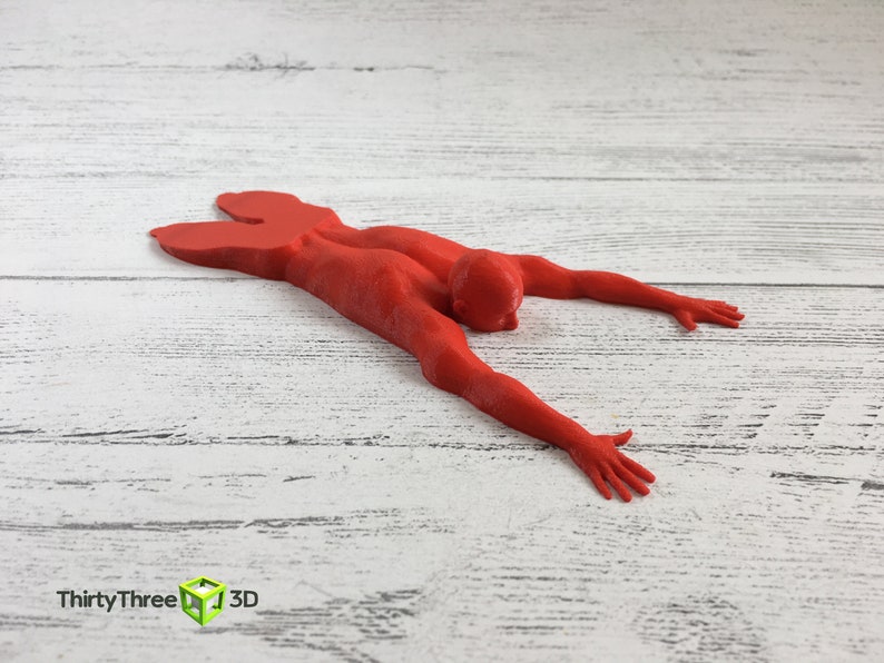 May include: A red 3D printed figurine of a person lying face down with arms outstretched.