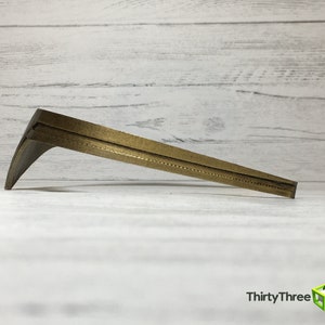 May include: A gold-colored metal bracket with a curved shape and a textured surface. The bracket is designed to support a shelf or other object.