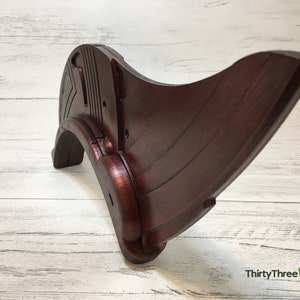 May include: A dark red wooden decorative piece with a curved shape and intricate details. The piece has a smooth, polished finish and appears to be handcrafted.
