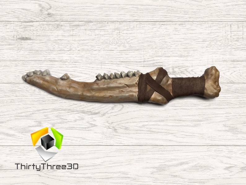 May include: A detailed replica of a bone weapon, featuring a jawbone with teeth and a wrapped handle. The prop is a light brown colour with dark brown wrappings, ideal for cosplay or display.