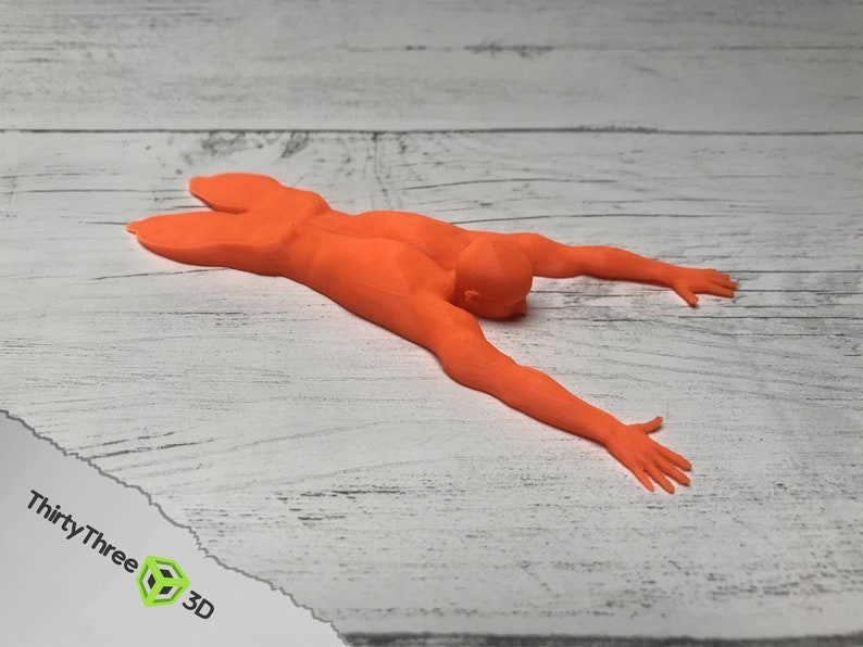 May include: Orange 3D printed figurine of a person lying on their stomach with arms outstretched.
