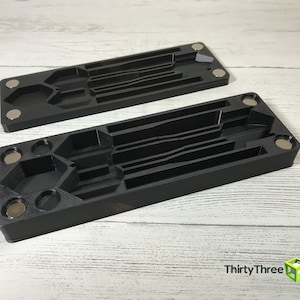 May include: Two black plastic magnetic storage boxes with multiple compartments for organizing small items. The boxes are empty and have a textured surface.