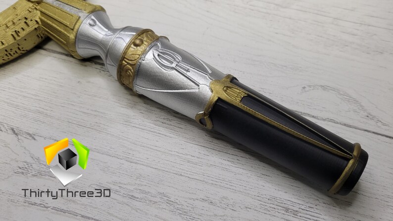 May include: A close-up of a silver and black decorative staff with gold accents. The staff has a detailed design with a symbol on the silver portion.