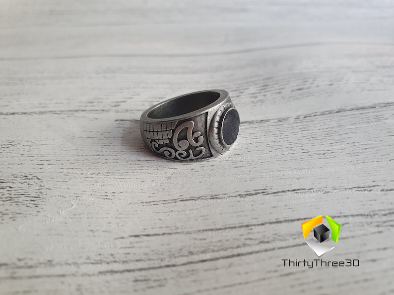 May include: A silver ring with an ornate design and a black stone in the center.