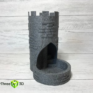 May include: A gray stone tower-shaped dice rolling tower with a rounded base and a small arched opening. The tower is textured to look like stone.
