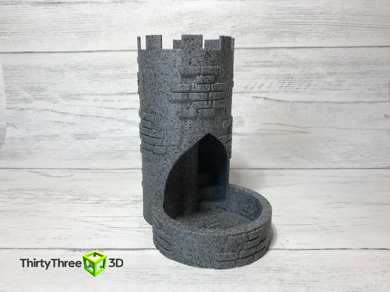 May include: A gray stone tower-shaped dice rolling tower with a rounded base and a small arched opening. The tower is textured to look like stone.