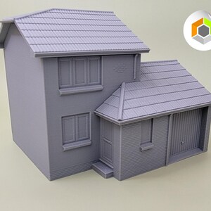 May include: A gray 3D printed model of a two-story house with a garage. The house has a pitched roof, windows, and a door. The garage has a door that is partially open.