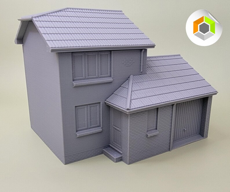 May include: A gray 3D printed model of a two-story house with a garage. The house has a pitched roof, windows, and a door. The garage has a door that is partially open.