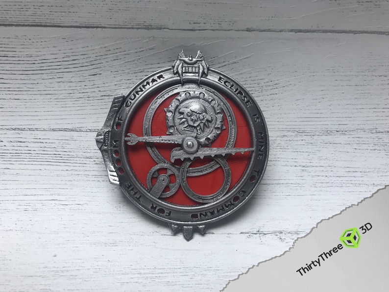 May include: A silver metal circular pendant with a red center and intricate gears. The pendant has the text "DOOM OF GUNMAR ECLIPSE IS MINE TO COMMAND" around the edge.