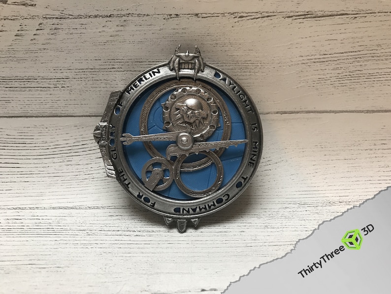 May include: A silver-colored metal pendant with a blue center and intricate gears. The text "FOR THE GLORY OF MERLIN DAYLIGHT IS MINE TO COMMAND" is inscribed around the edge.