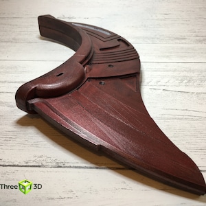 May include: A dark red, curved, plastic prop with a textured surface and a geometric design. The prop is shaped like a fin or wing.
