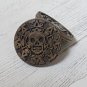 May include: Two gold-colored metal coins with a skull and crossbones design. The coins are stacked on top of each other.