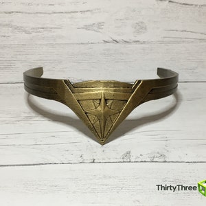 May include: A gold-colored headband with a star-shaped design in the center. The headband is made of metal and has a smooth finish.