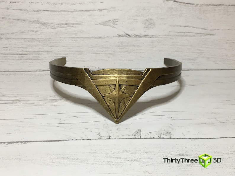 May include: A gold-colored headband with a star-shaped design in the center. The headband is made of metal and has a smooth finish.