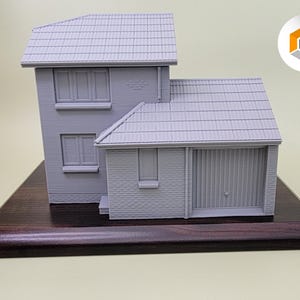 May include: A gray 3D printed model of a house with a garage door on a dark wood base.