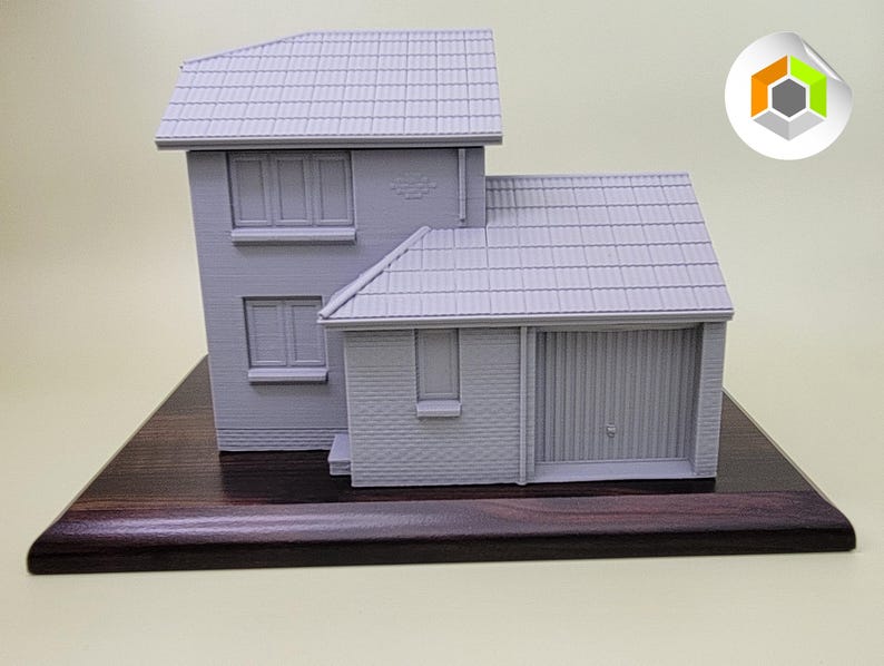 May include: A gray 3D printed model of a house with a garage door on a dark wood base.