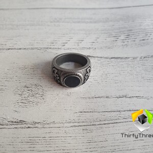 May include: A silver ring with an ornate design and a black stone in the center.