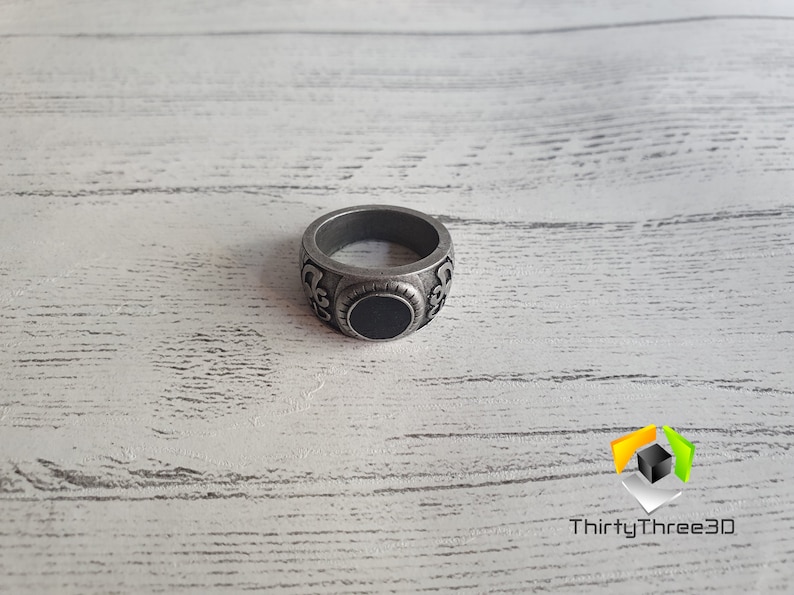 May include: A silver ring with an ornate design and a black stone in the center.