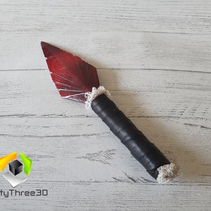May include: A handmade decorative knife with a red blade and a black wrapped handle. The blade has a feather-like design with white accents. The handle is wrapped in black material and has a white trim at the base of the blade.