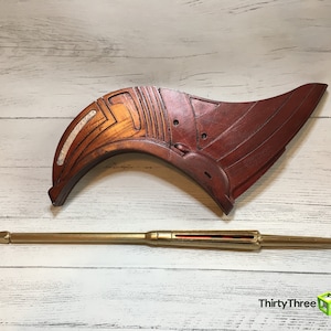 May include: A wooden, red and white, curved, decorative piece with a gold metal spear.  ThirtyThree 3D is printed on the bottom right corner of the image.