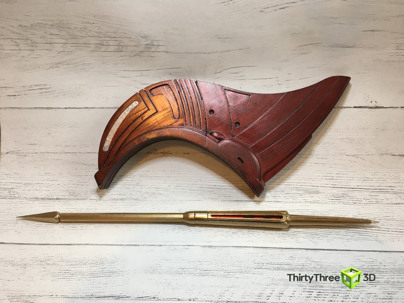 May include: A wooden, red and white, curved, decorative piece with a gold metal spear.  ThirtyThree 3D is printed on the bottom right corner of the image.