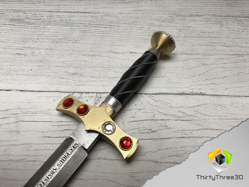 May include: A gold and silver sword with a black handle and red gems. The sword has a inscription that reads "SEC FIRIS VISII".