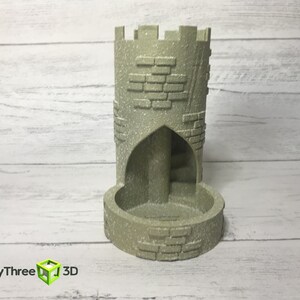 May include: A gray stone tower-shaped dice tower with a brick pattern and a rounded base. The tower has a small archway opening on one side.