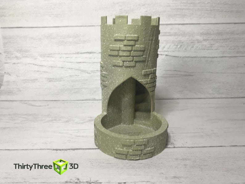 May include: A gray stone tower-shaped dice tower with a brick pattern and a rounded base. The tower has a small archway opening on one side.