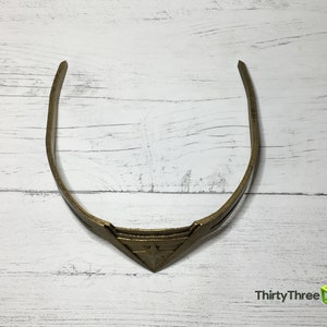May include: A gold-colored headband with a triangular design in the center. The headband is made of a thin, flexible material.