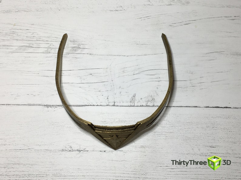 May include: A gold-colored headband with a triangular design in the center. The headband is made of a thin, flexible material.
