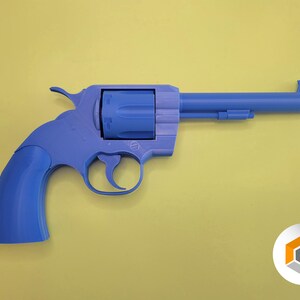 Op de afbeelding: Een blauwe speelgoedrevolver met een oranje punt, tegen een gele achtergrond. Het speelgoedpistool is een gedetailleerde replica, met een trekker, hamer en cilinder. Het algehele ontwerp is een klassieke westernstijl.