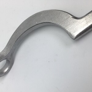 Puede incluir: Una llave de metal plateada con un mango curvo y una abertura circular en un extremo.