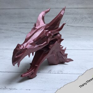 May include: A 3D printed dragon head sculpture in a metallic red finish. The sculpture is detailed with sharp teeth and scales.